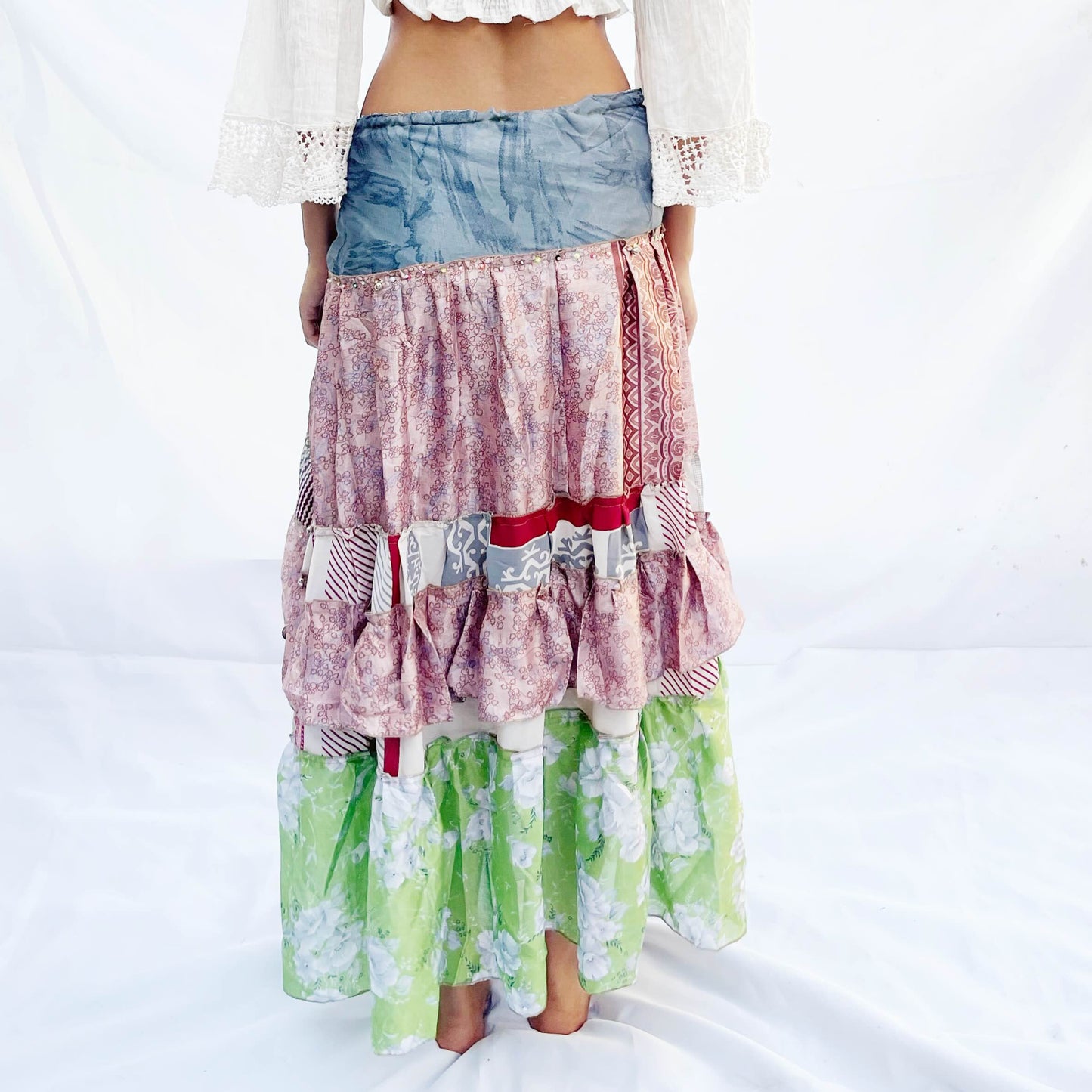 A vibrant patchwork skirt crafted from vintage sari fabric, featuring shades of blue, pink, and green with intricate floral and geometric patterns. It includes a drawstring for an adjustable fit.
