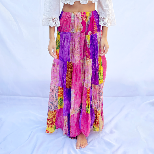 A colorful vintage silk sari skirt with an elastic band, featuring a patchwork of vibrant pink, purple, and yellow tones. The flowing design offers a comfortable and stylish fit.