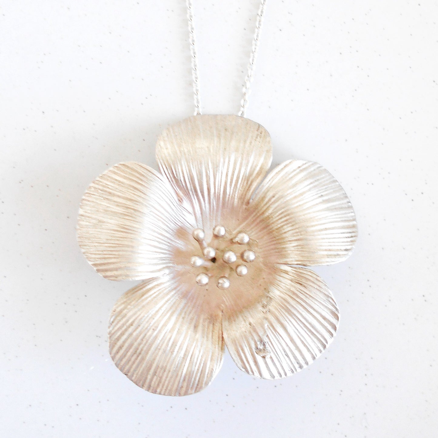 Close-up of a large Vintage Sterling Silver flower pendant necklace being worn. Pendant features textured petals and silver bead details in the center, hanging on a silver chain. Handcrafted by Nepalese artisans for Dilmaya Gifts.