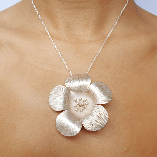 Close-up of a large Vintage Sterling Silver flower pendant necklace being worn. Pendant features textured petals and silver bead details in the center, hanging on a silver chain. Handcrafted by Nepalese artisans for Dilmaya Gifts.