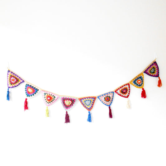 Hand-crocheted bunting made of colorful, patterned triangles strung together, each with a small tassel at the point, displayed against a plain white background. Ethically crafted by Nepalese women artisans for Dilmaya Gifts.