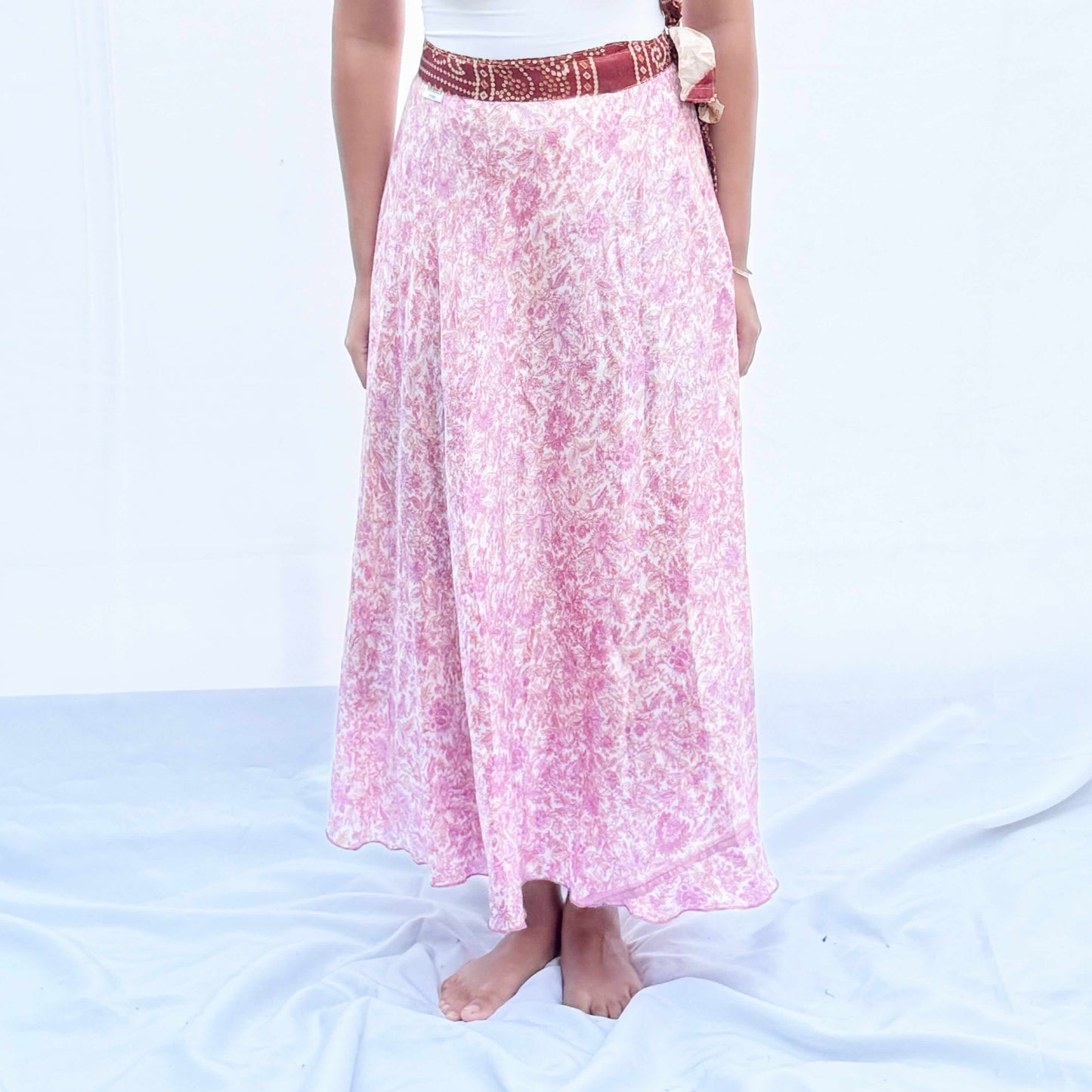 A unique skirt crafted from vintage rayon sari fabric, featuring a delicate pink floral pattern with a traditional maroon border. This flowing wrap design offers an elegant, adjustable fit and is reversible.