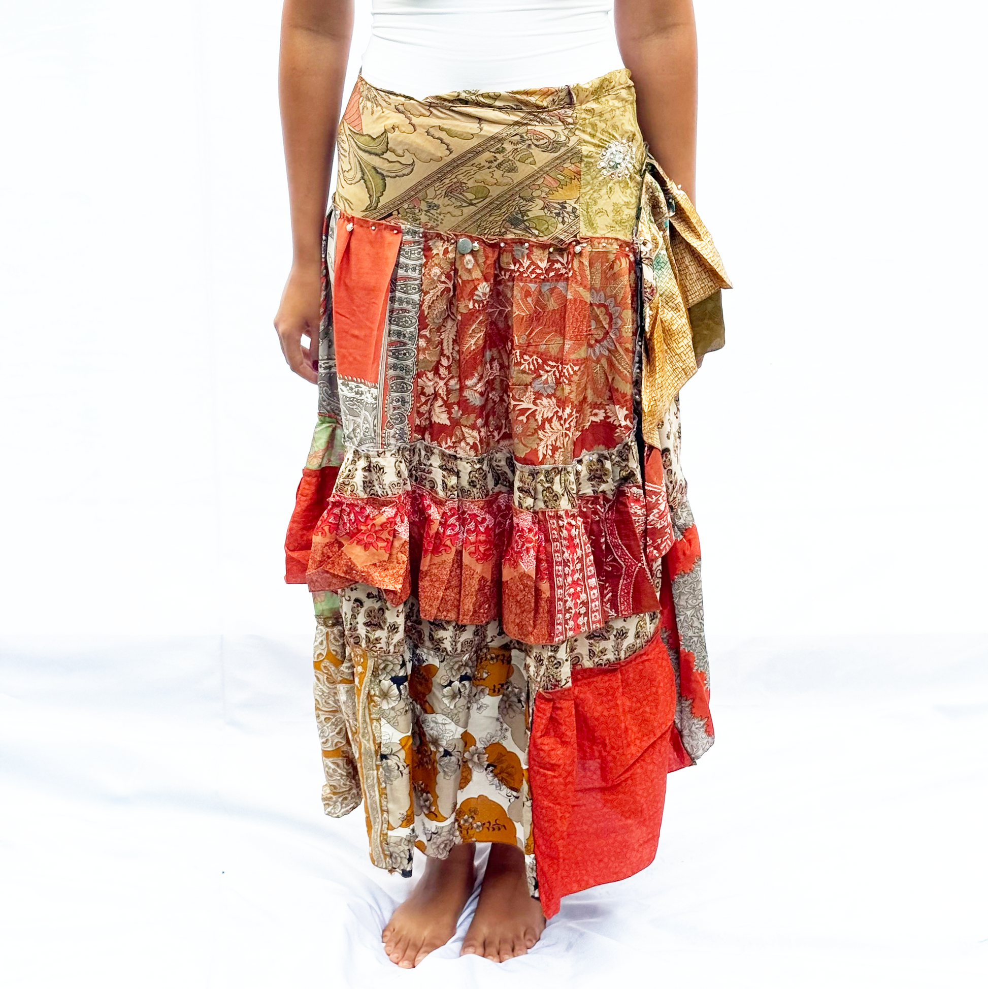 A vibrant patchwork skirt made from vintage saris, featuring warm earthy tones of red, orange, and beige. It has an adjustable drawstring for a customisable fit.