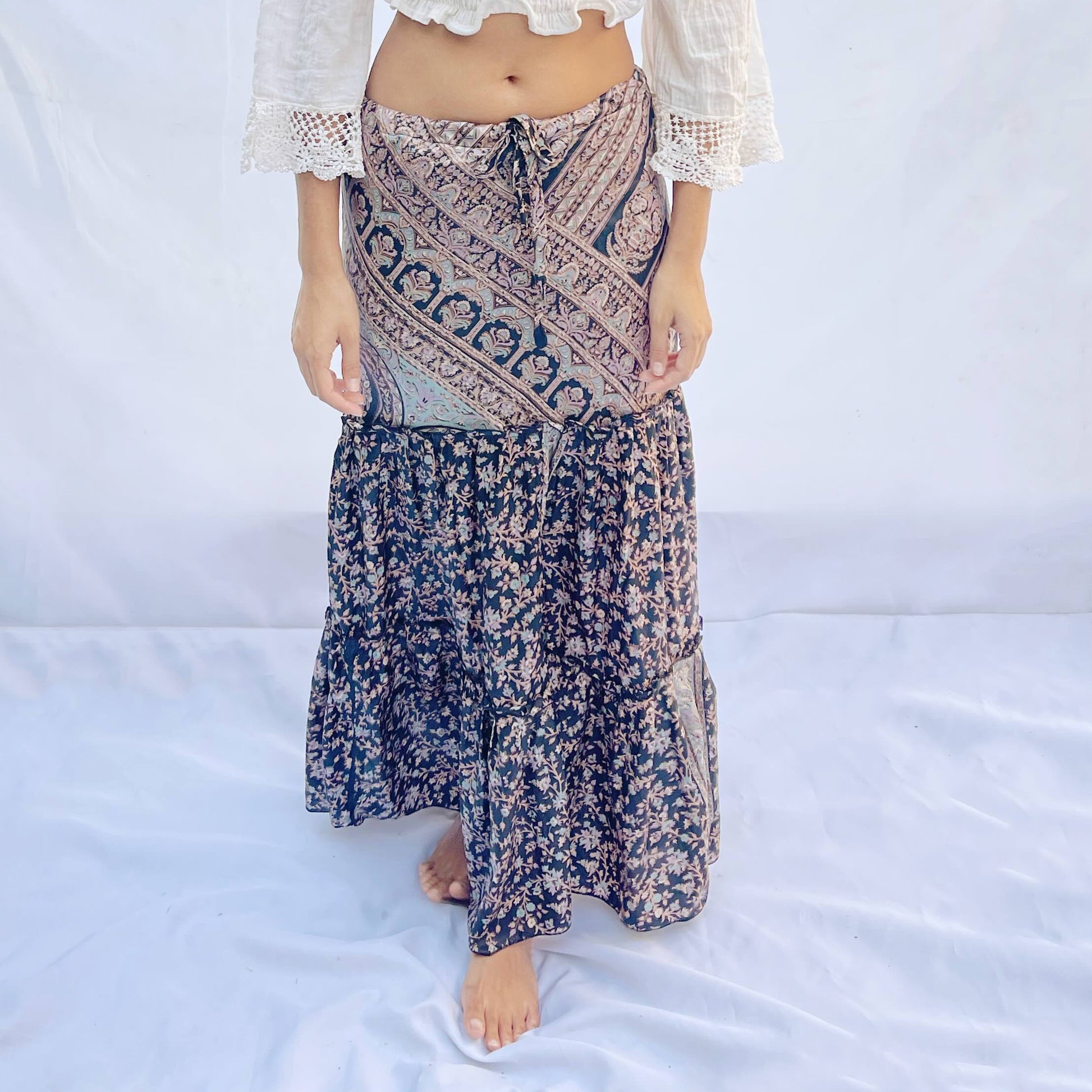 A drawstring skirt made from vintage sari fabric, featuring intricate patterns in shades of black, beige, and blue with floral designs. The adjustable fit adds elegance and comfort.