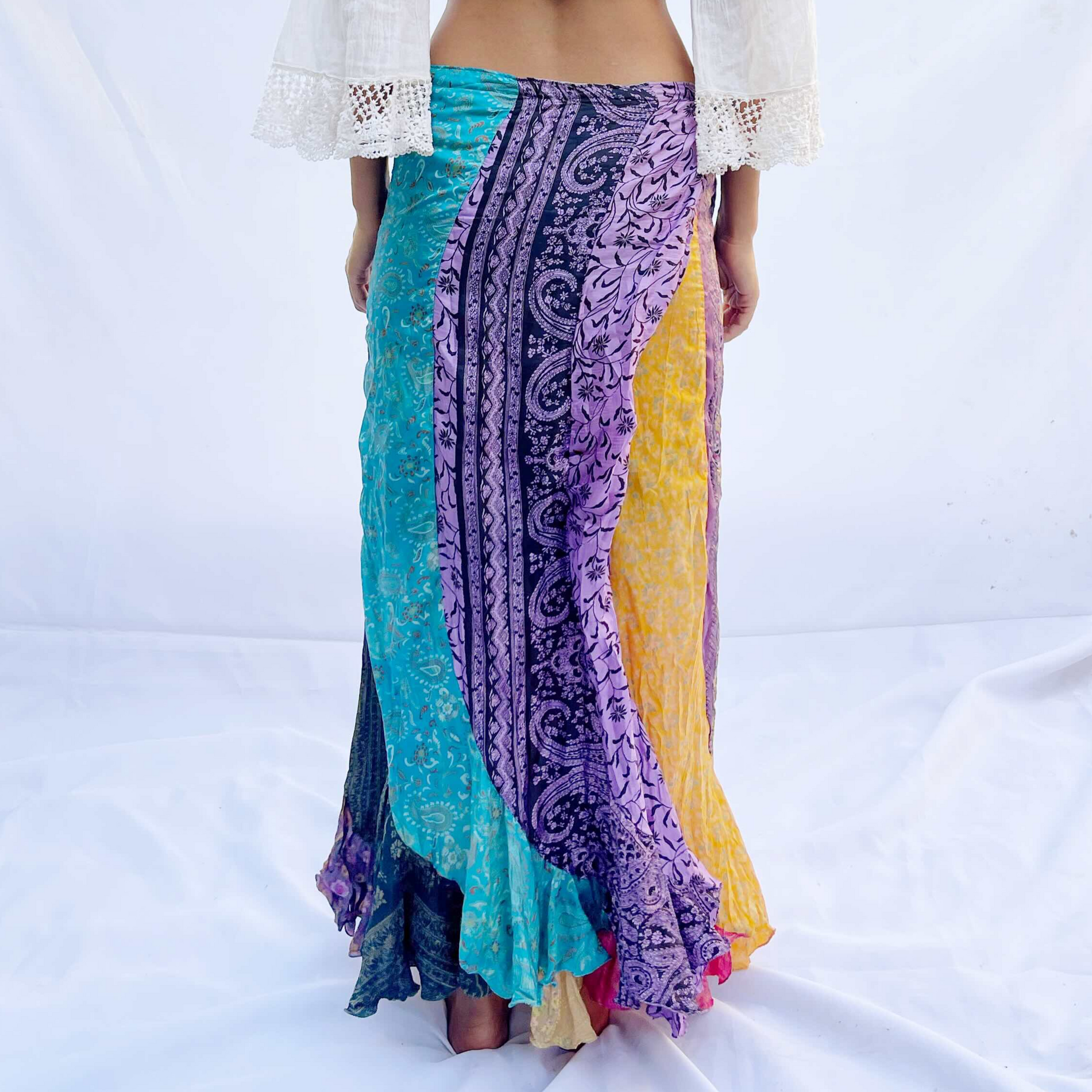 A reversible wrap skirt made from vintage sari fabric, featuring flowing panels in vibrant shades of purple, yellow, and green. The design offers versatility and elegance.