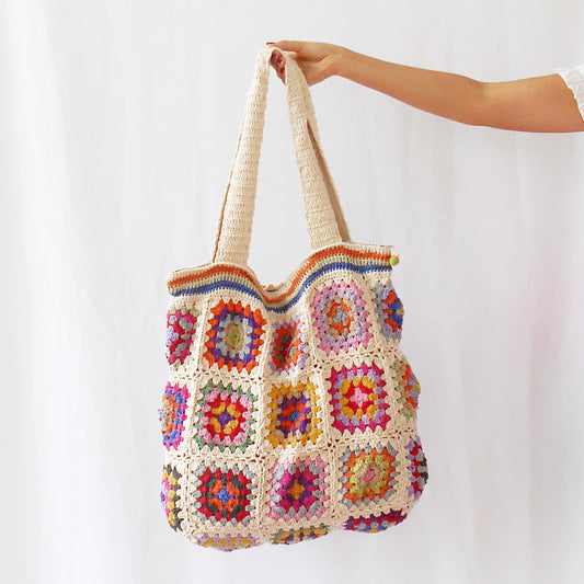 Handcrafted cotton crochet bag in grey-blue with colourful granny squares featuring yellow, orange, pink, and purple patterns, held against white background with natural shadows
