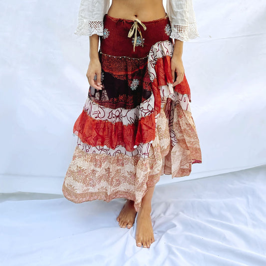 A vintage drawstring skirt crafted from sari fabric, featuring rich shades of red, black, and beige with intricate patterns. The design is flowy and adjustable for a comfortable fit.