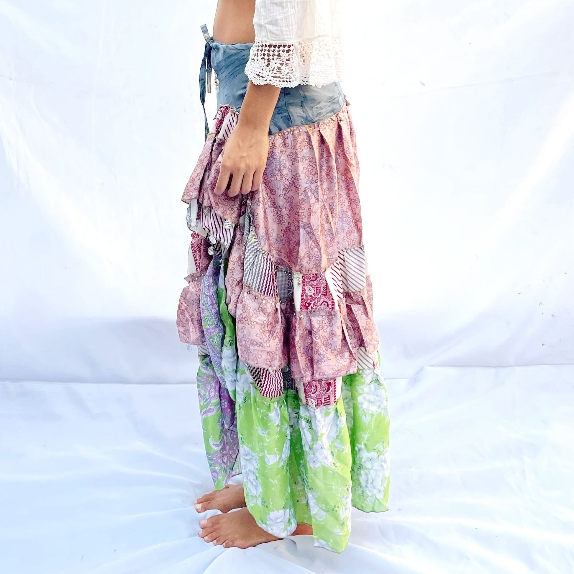 A vibrant patchwork skirt crafted from vintage sari fabric, featuring shades of blue, pink, and green with intricate floral and geometric patterns. It includes a drawstring for an adjustable fit.