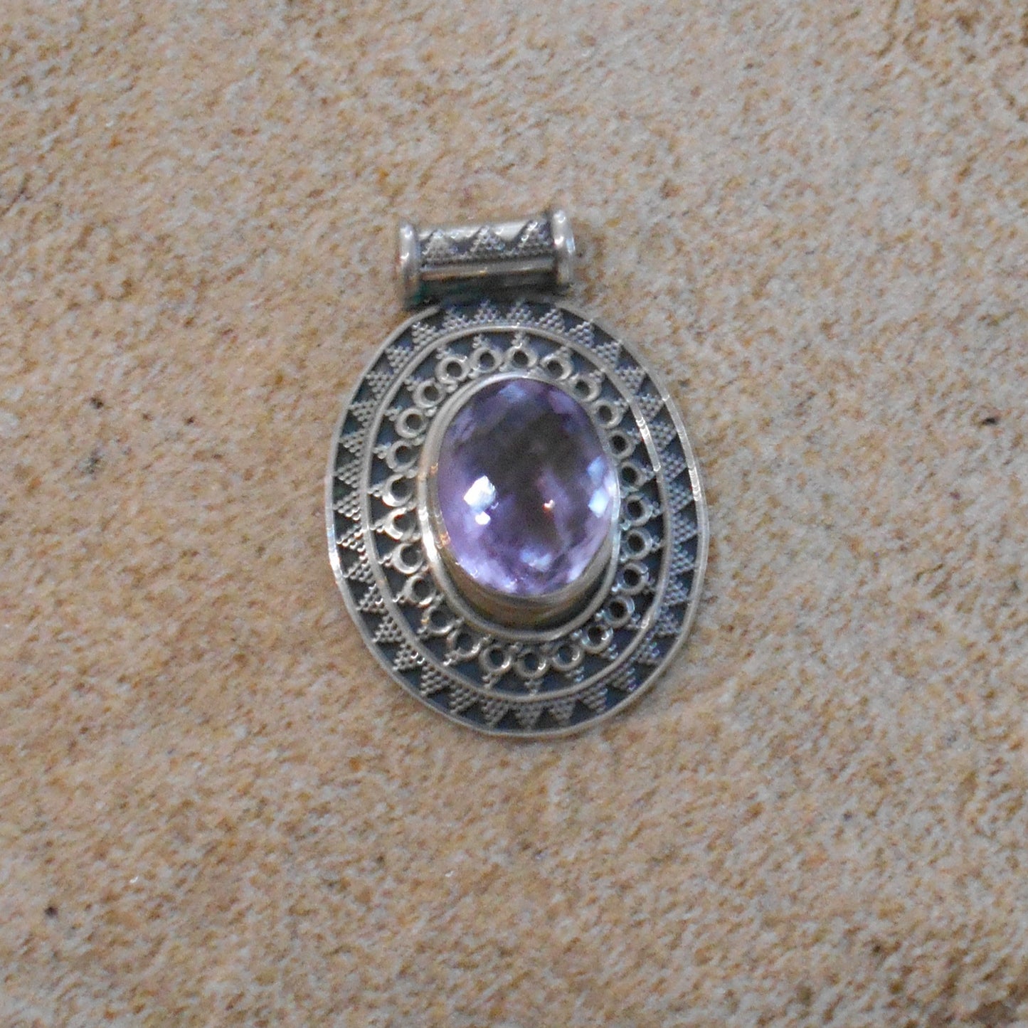 Vintage 925 sterling silver pendant featuring oval amethyst stone with intricate filigree border, photographed on textured beige surface