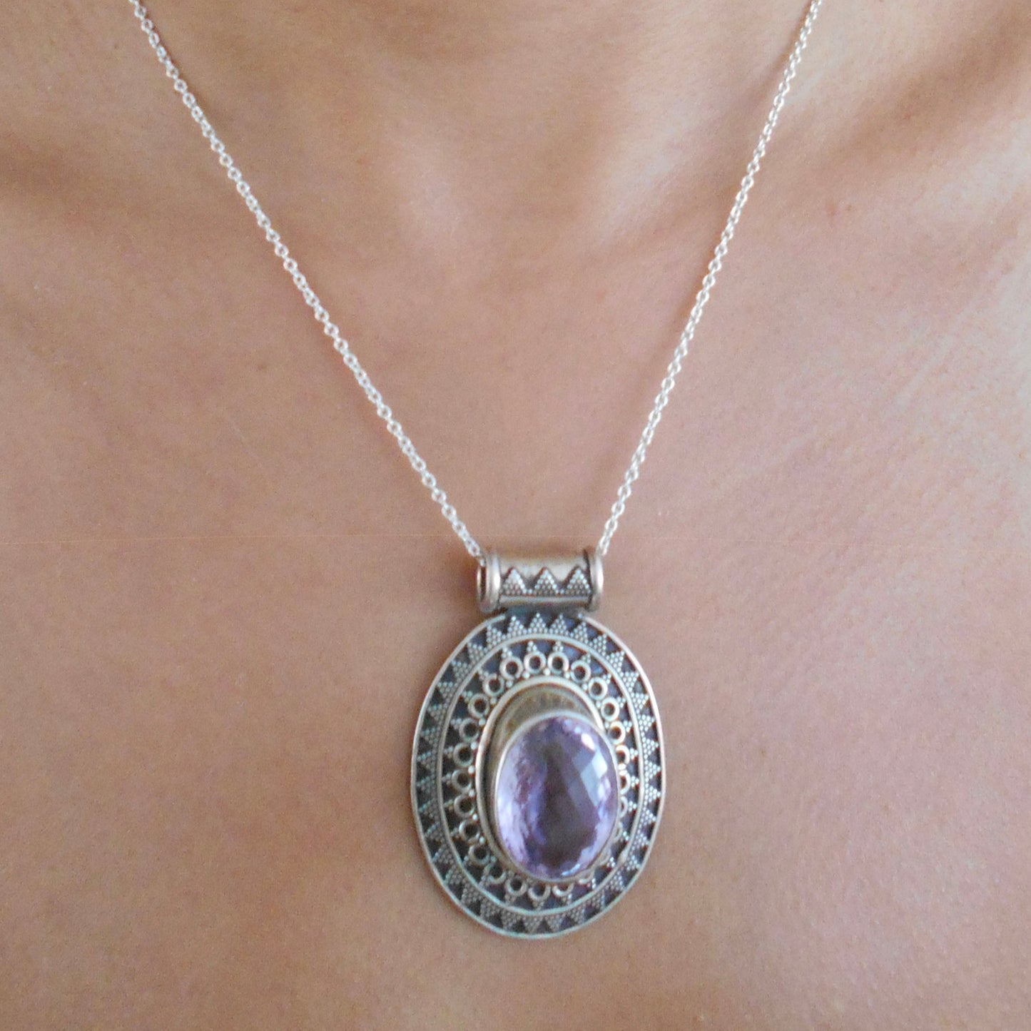 Vintage 925 sterling silver pendant featuring oval amethyst stone with intricate filigree border, photographed on textured beige surface