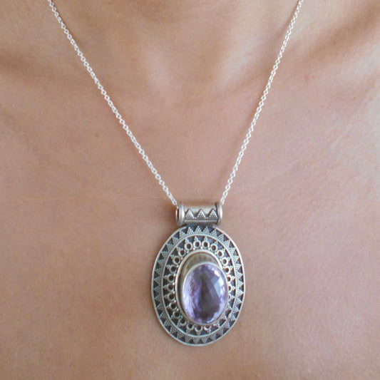 Vintage 925 sterling silver pendant featuring oval amethyst stone with intricate filigree border, photographed on textured beige surface