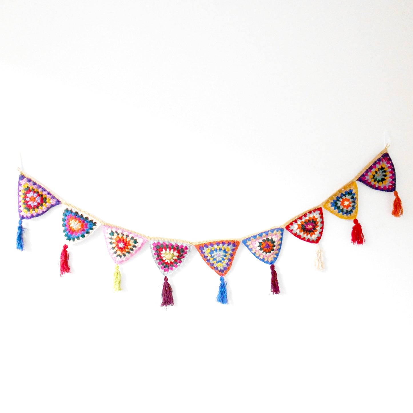 Hand-crocheted bunting made of colorful, patterned triangles strung together, each with a small tassel at the point, displayed against a plain white background. Ethically crafted by Nepalese women artisans for Dilmaya Gifts.