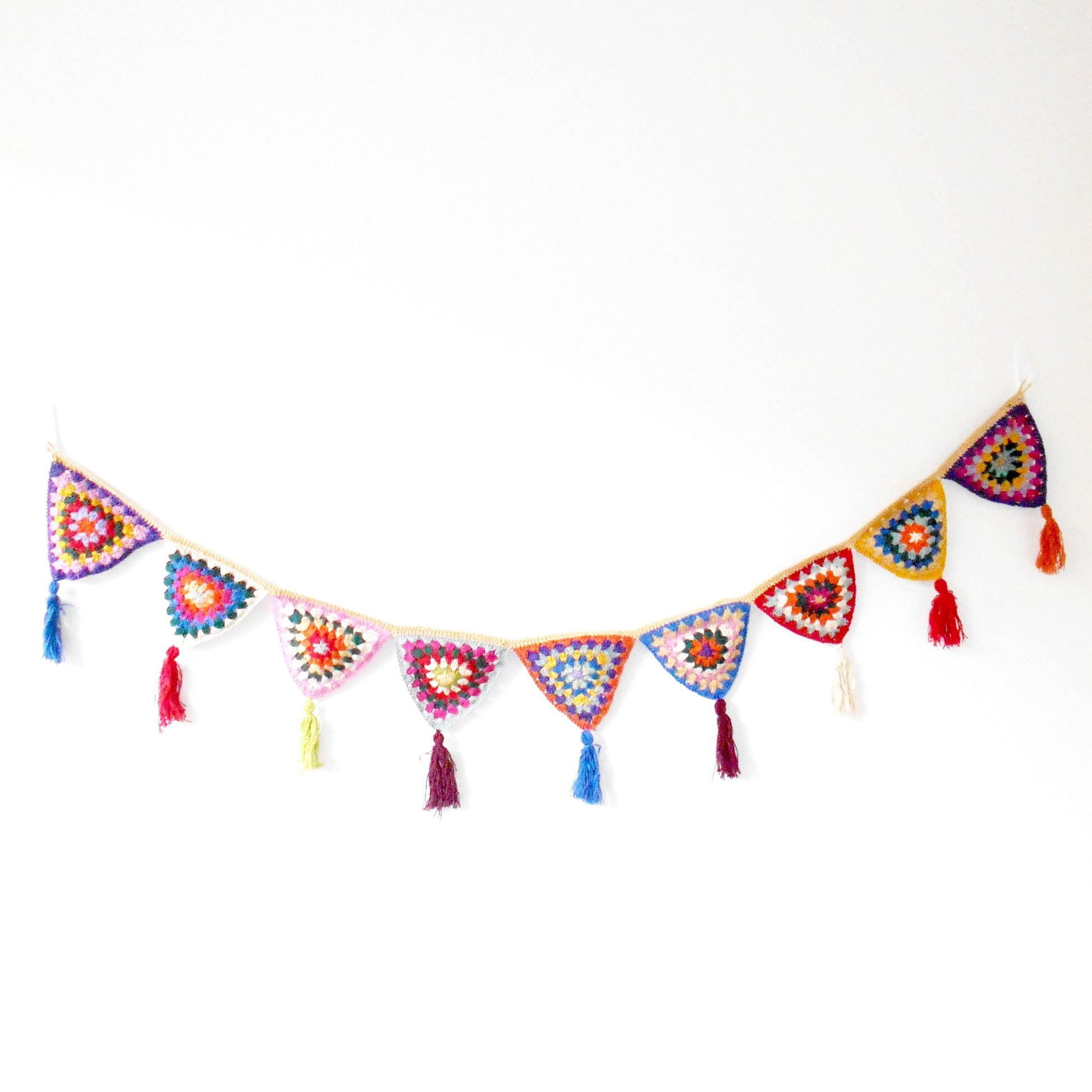 Hand-crocheted bunting made of colorful, patterned triangles strung together, each with a small tassel at the point, displayed against a plain white background. Ethically crafted by Nepalese women artisans for Dilmaya Gifts.