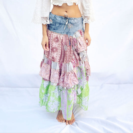 A vibrant patchwork skirt crafted from vintage sari fabric, featuring shades of blue, pink, and green with intricate floral and geometric patterns. It includes a drawstring for an adjustable fit.