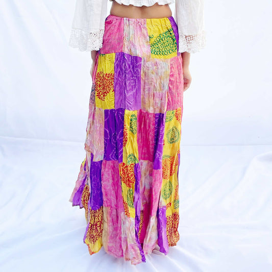 A colourful vintage silk sari skirt with an elastic band, featuring a patchwork of vibrant pink, purple, and yellow tones. The flowing design offers a comfortable and stylish fit.