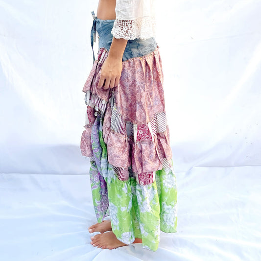 A vibrant patchwork skirt crafted from vintage sari fabric, featuring shades of blue, pink, and green with intricate floral and geometric patterns. It includes a drawstring for an adjustable fit.