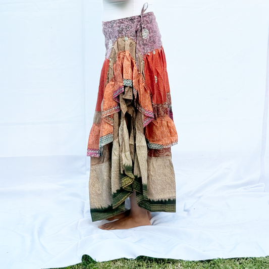 A vibrant patchwork skirt made from vintage saris, featuring shades of orange, pink, beige, and green with intricate patterns. The skirt includes an adjustable drawstring for a customisable fit.